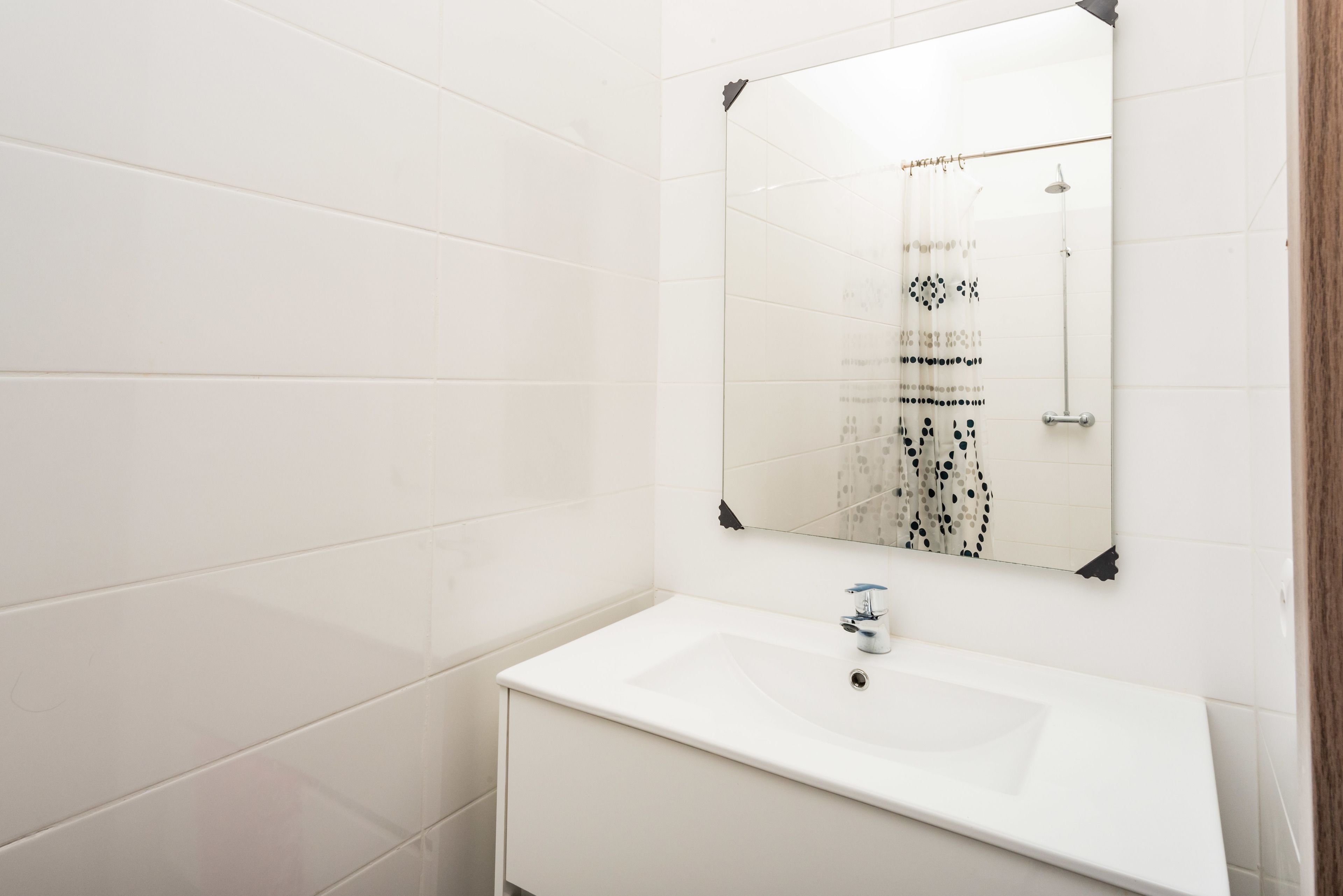 A bathroom with white tiles, a white sink, and a mirror.