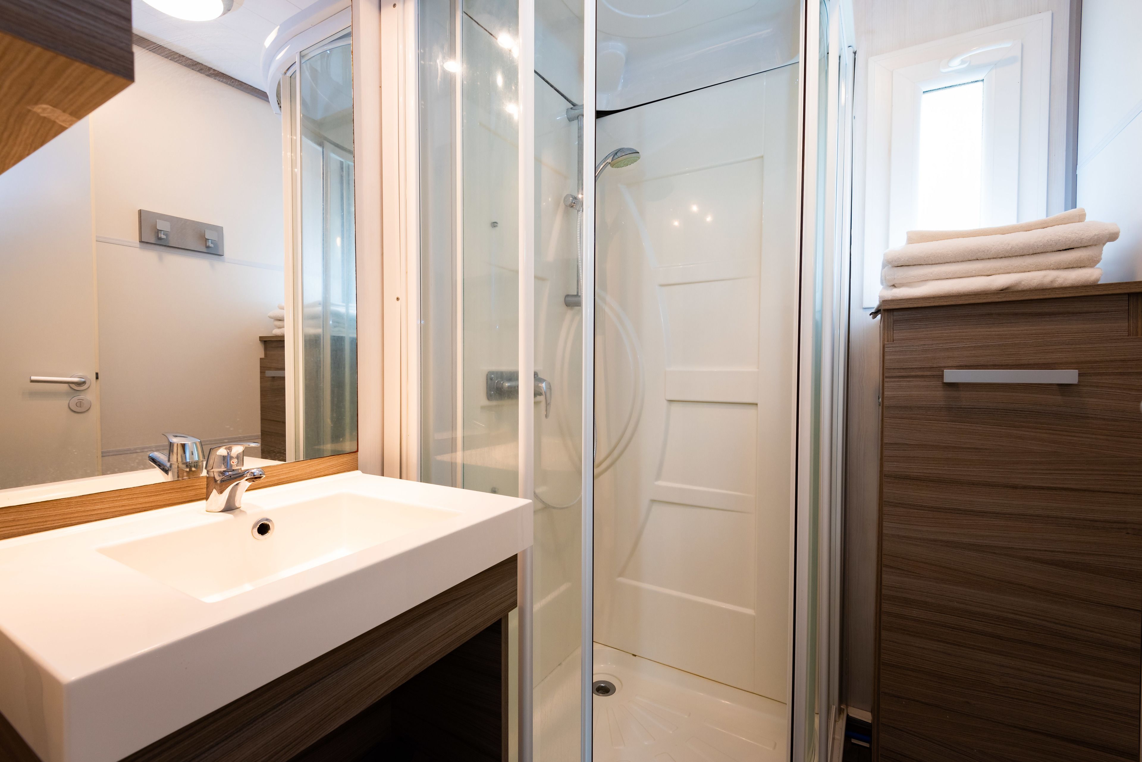 A modern bathroom with a glass-enclosed shower, a white sink, and wooden cabinetry.
