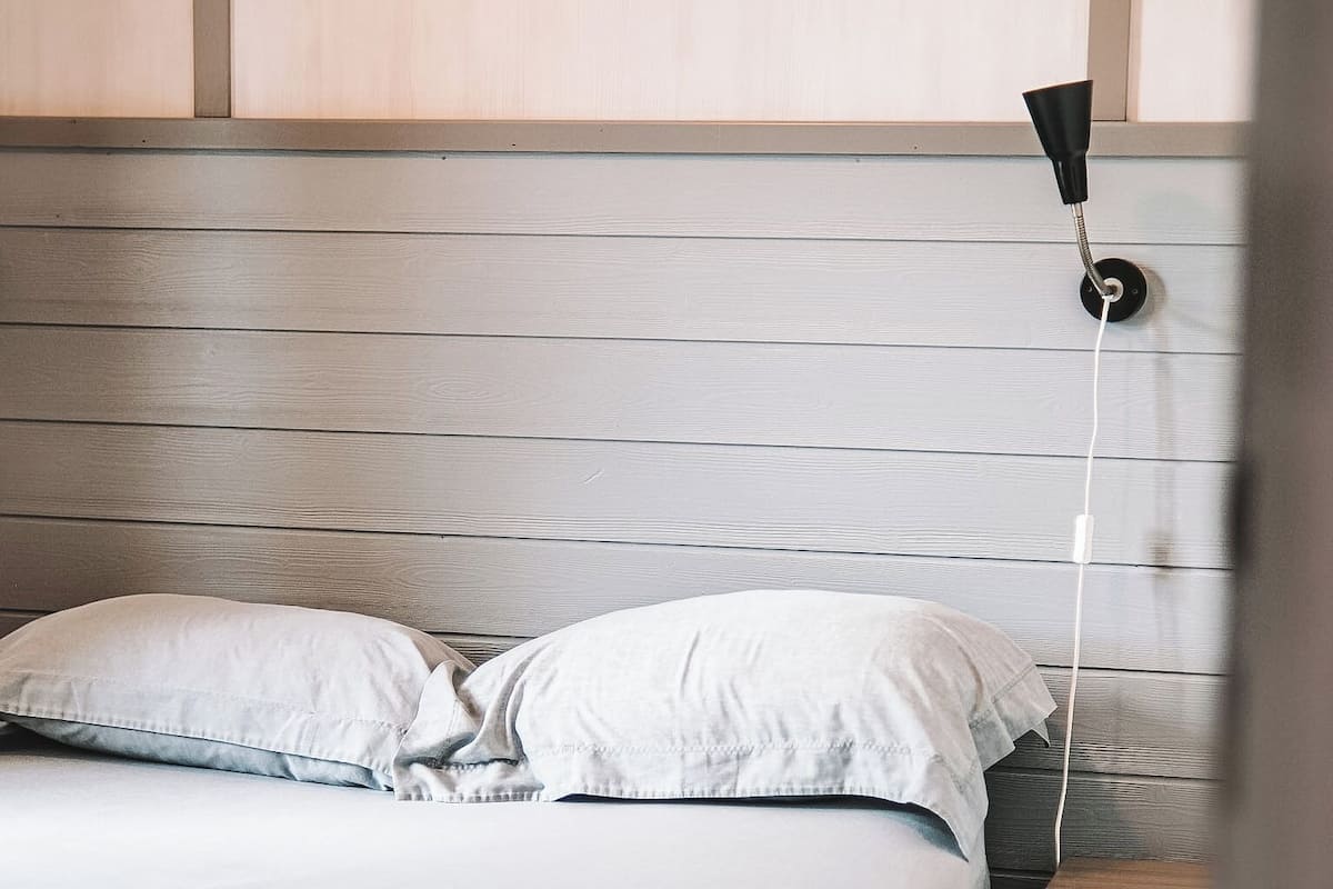 Ein Bett mit weißer Bettwäsche, ein Nachttisch mit Lampe und ein Holzkopfstück.