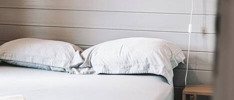 Una cama con ropa blanca, una mesita de noche con lámpara y un cabecero de madera.