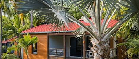 Una casa con techo rojo, rodeada de un césped cuidado y palmeras.