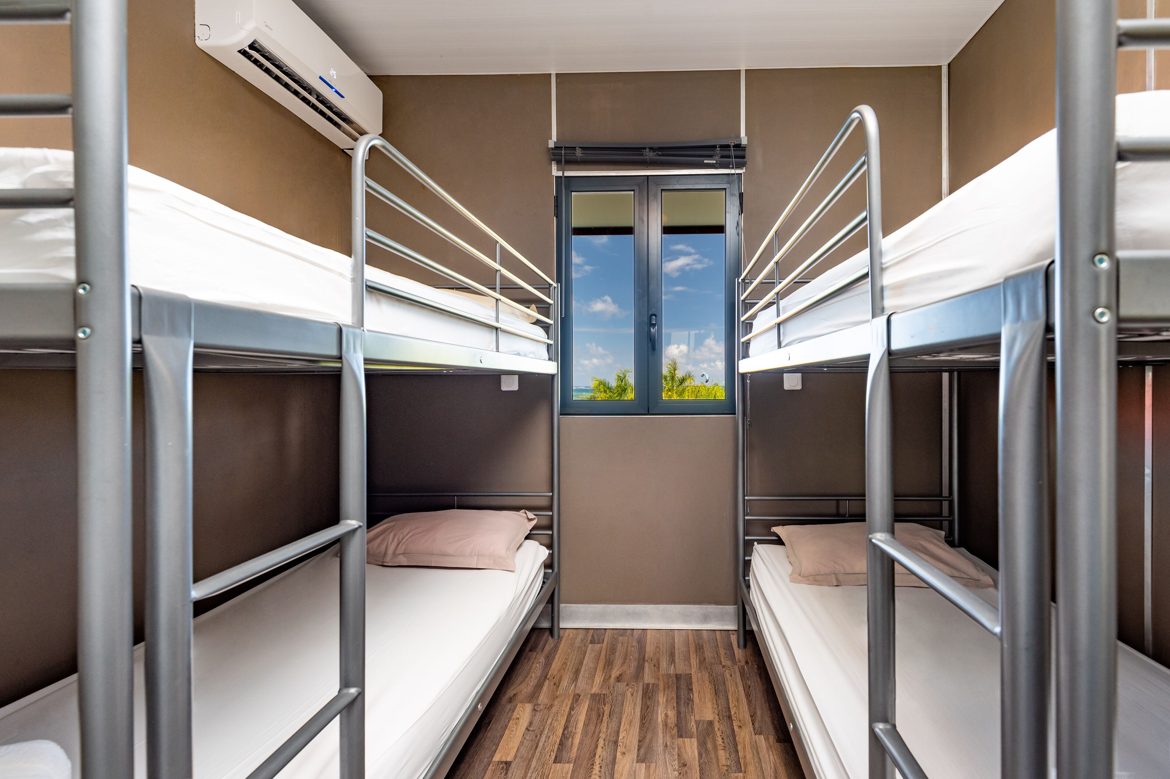 A bunk room with metal railings, a window, and a wooden floor.