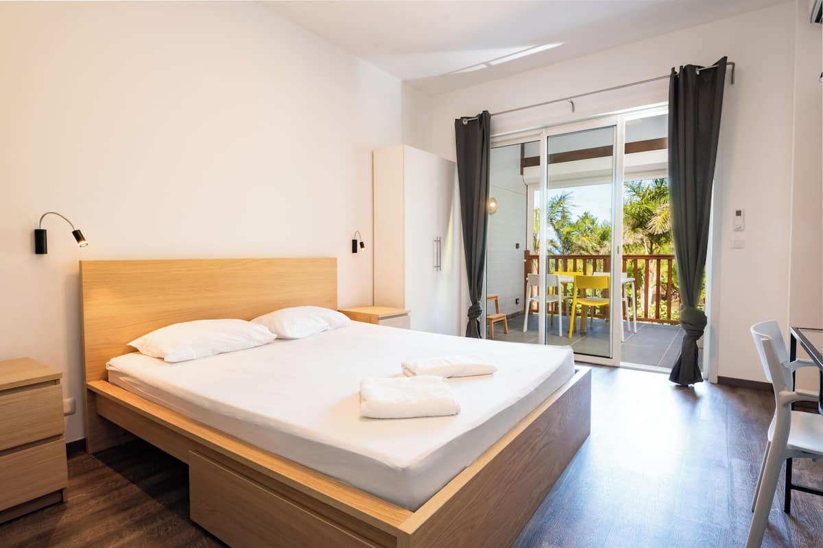 Ein modernes Hotelzimmer mit einem Holzbett, einem kleinen Nachttisch, einem Kleiderschrank und einem Balkon mit Sitzgelegenheit.