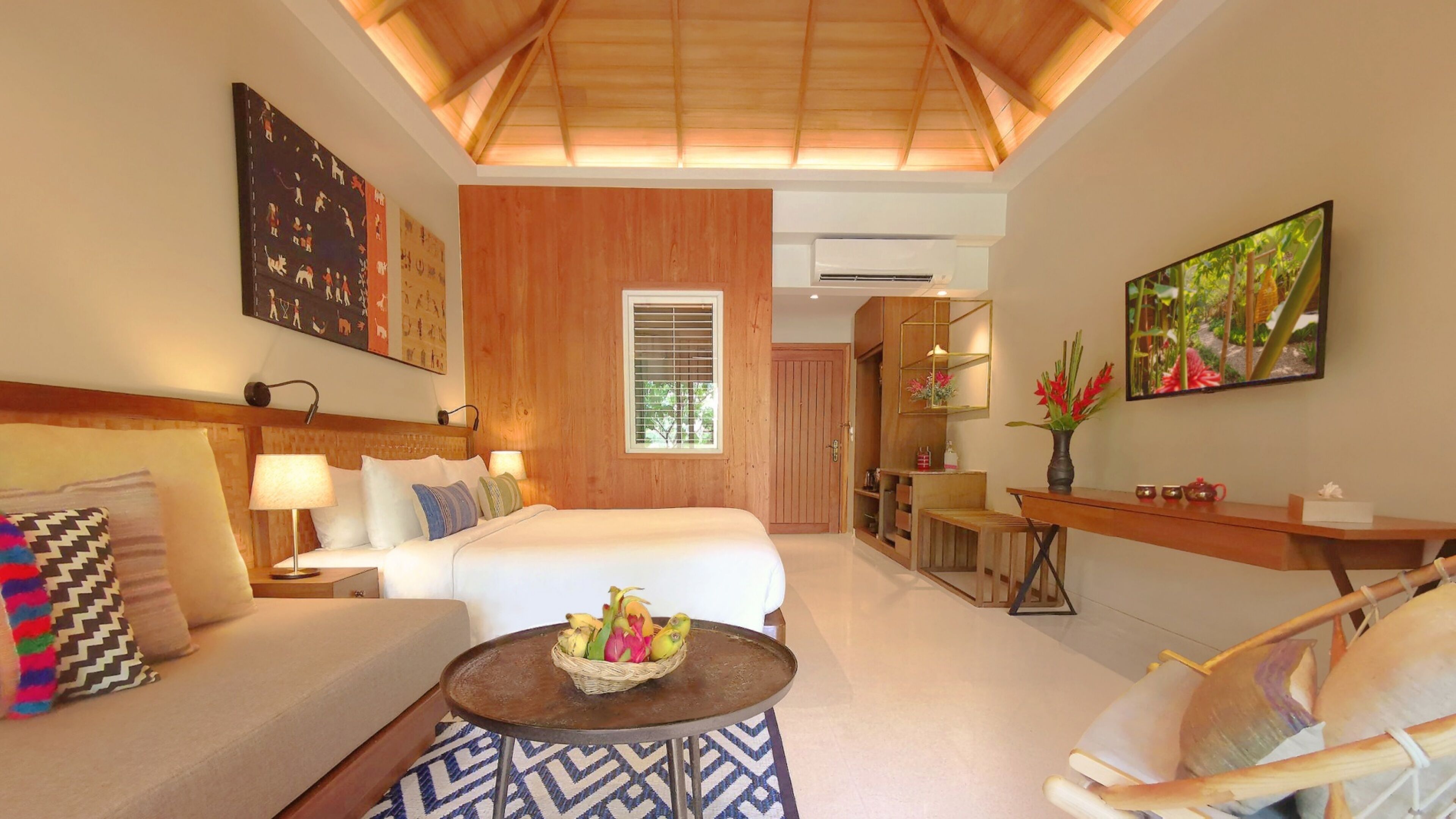 A hotel room with a bed, a sofa, a dining area, and artwork on the walls.