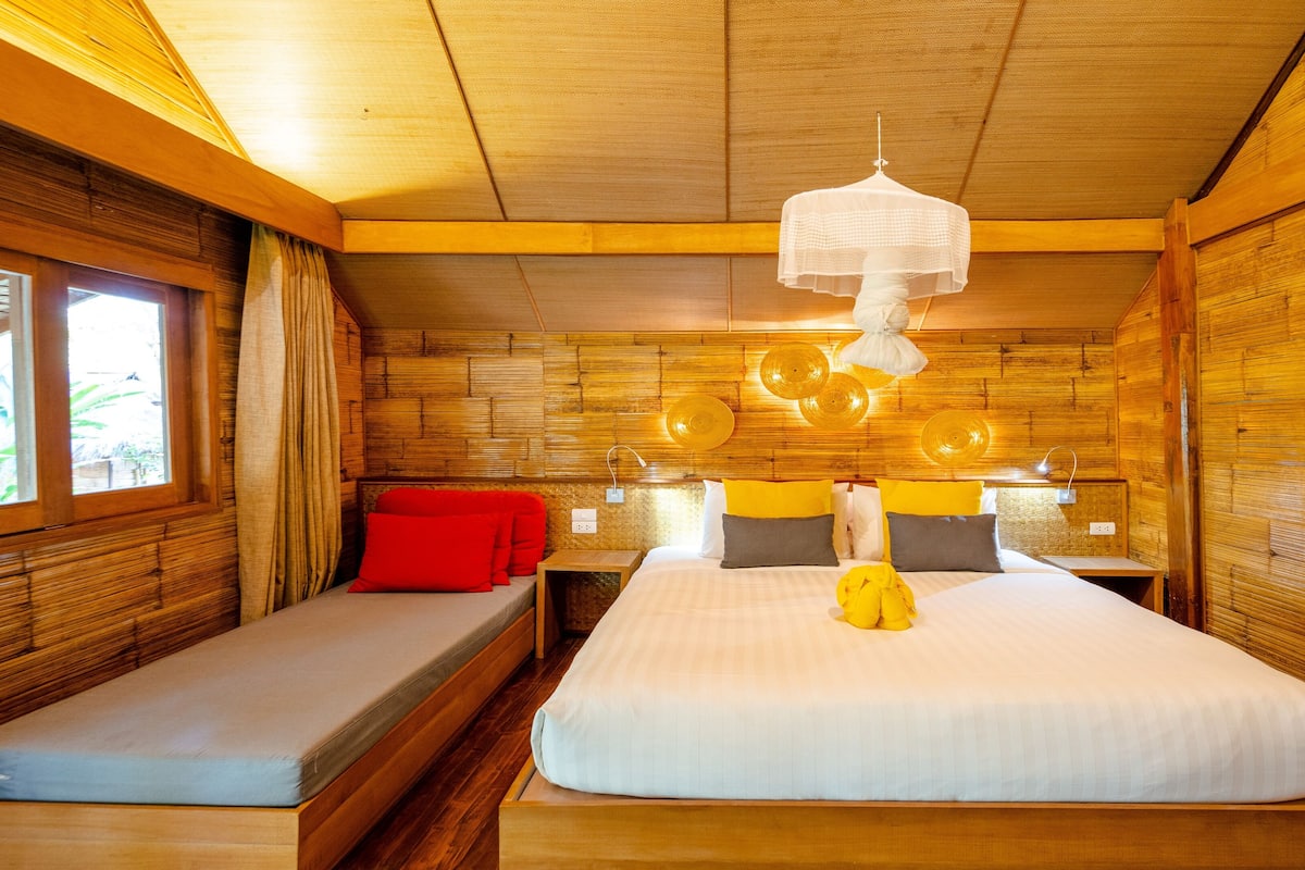 A wooden cabin-style room with two beds, a window with curtains, and a hanging light fixture.