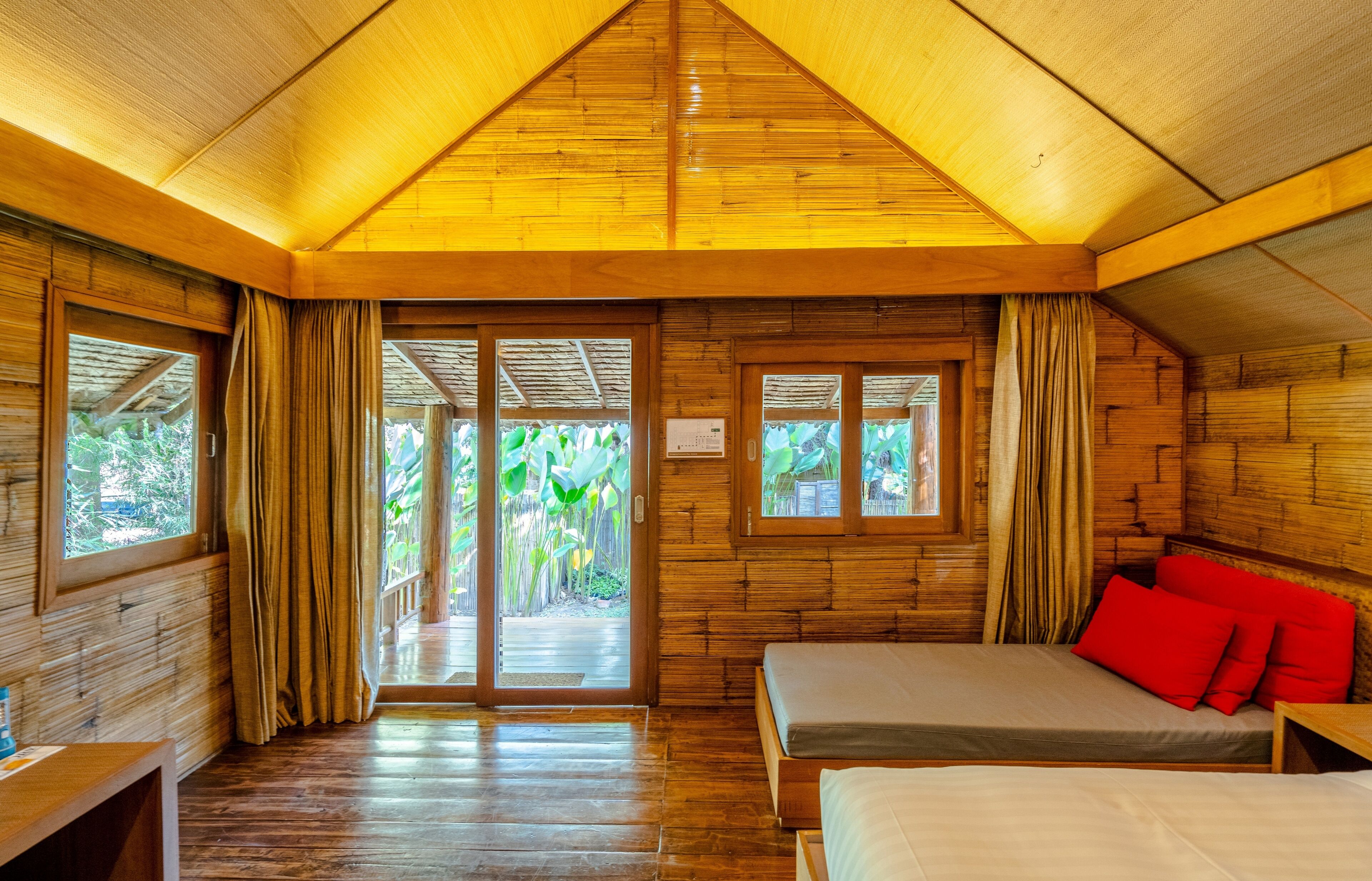 A wooden cabin with a bed, a bench, and a window with curtains.