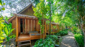 Uma cabana de madeira com varanda, rodeada por vegetação exuberante e um caminho de cascalho.