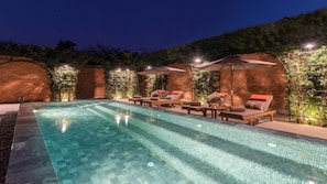 A swimming pool with lounge chairs and umbrellas, surrounded by brick walls and greenery. - Pai Village Boutique Resort (Pai)