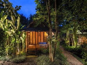 A wooden cabin with a porch, surrounded by dense foliage. - Pai Village Boutique Resort (Pai)