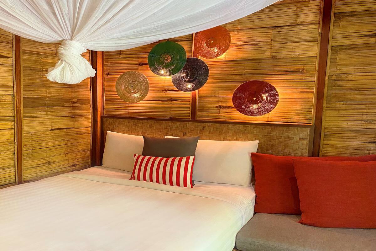A bed with white bedding, red and white striped pillows, and red pillows.