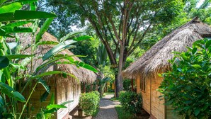 Uma trilha que conduz a cabanas com telhados de palha, cercadas por vegetação exuberante.