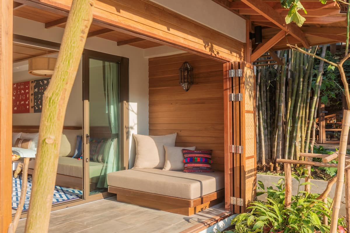 A cozy room with a bed, wooden ceiling beams, and a view of bamboo outside.