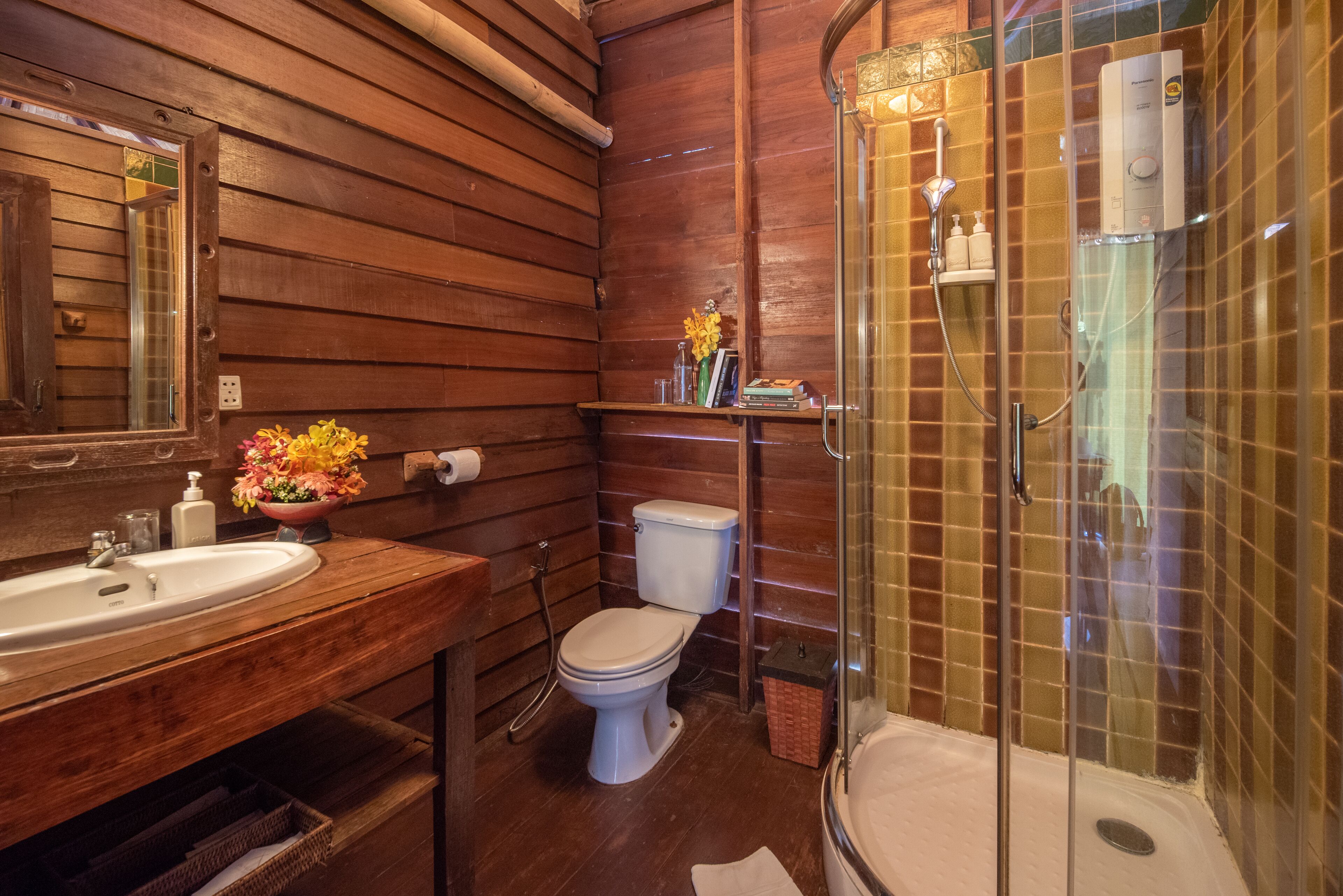Un baño de madera con lavamanos, inodoro y ducha con mampara de vidrio.