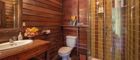 Un baño de madera con lavamanos, inodoro y ducha con mampara de vidrio.