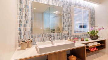 Un baño moderno con un espejo grande, un lavabo blanco y una ventana con persianas.