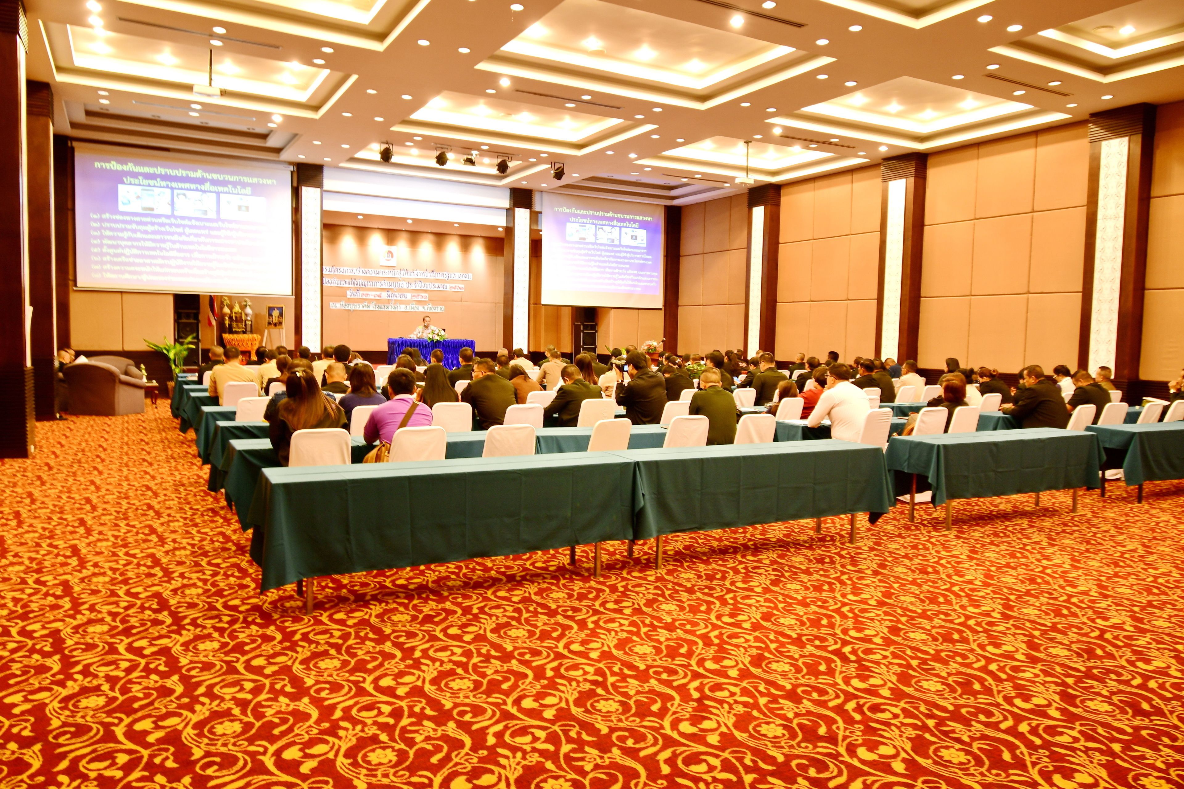 A conference room with rows of tables and chairs, a carpeted floor, and a large screen at the front.