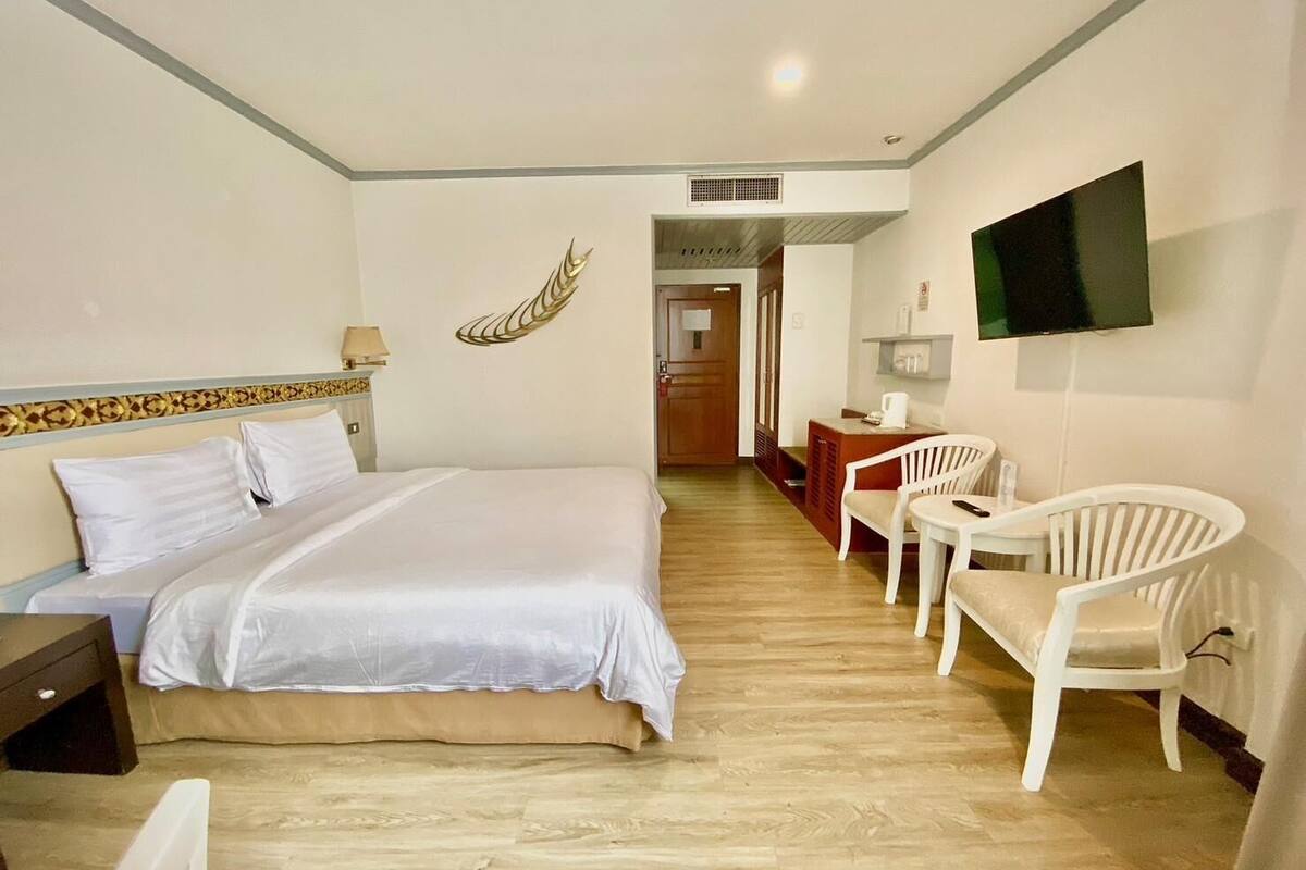 A hotel room with a bed, a desk, a chair, a television, and a decorative wall piece.