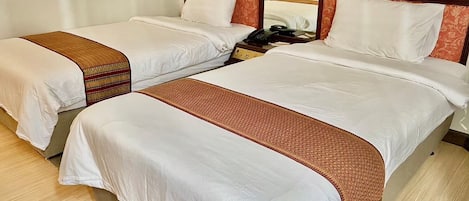 Habitación de hotel con dos camas, cada una con ropa blanca y un corredor estampado. Cuenta con un cabecero de madera con un diseño decorativo y dos lámparas de noche.
