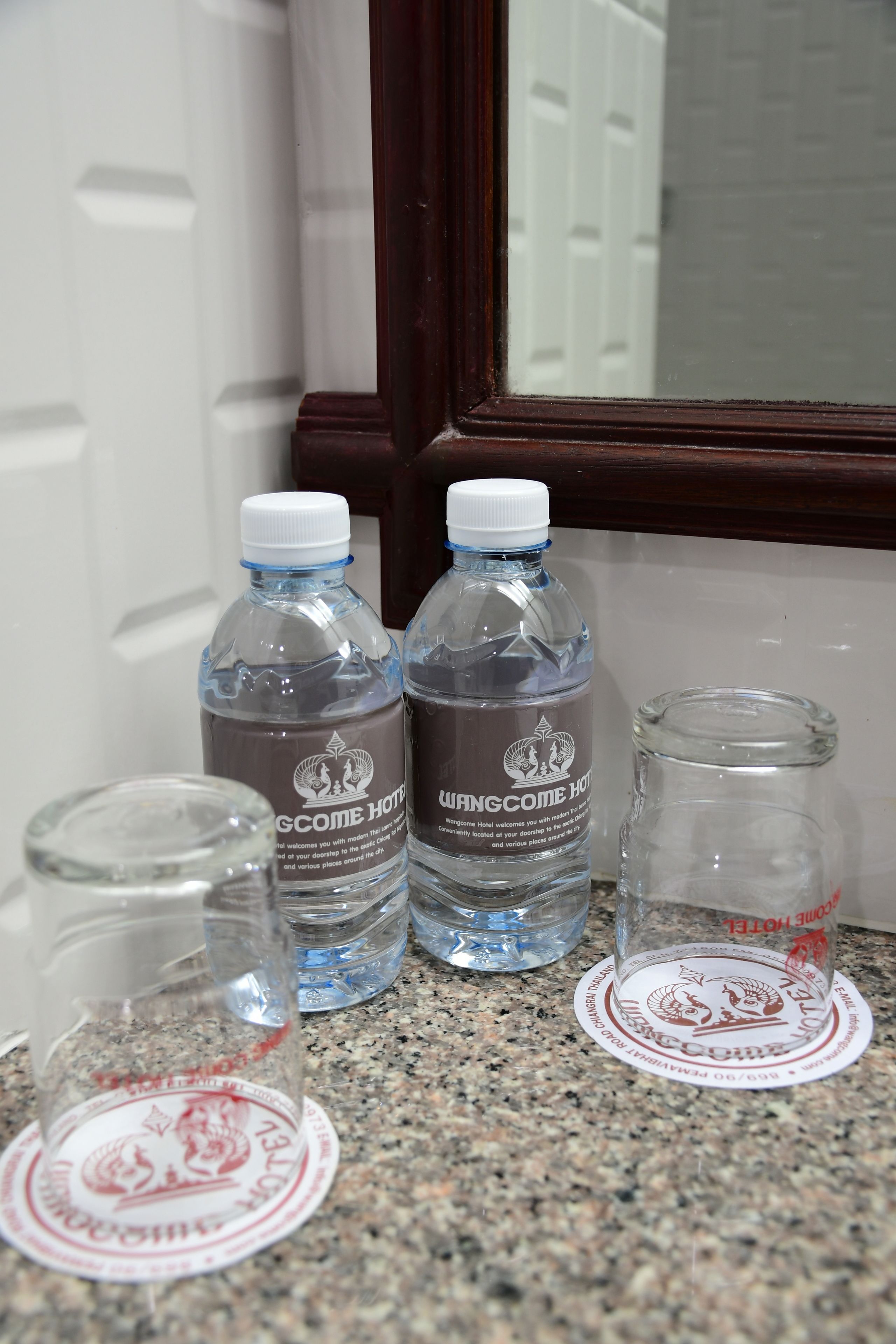 Two water bottles with labels on a granite countertop near a window with a wooden frame.