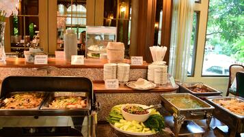 Uma mesa de buffet com diversos pontos de serviço de comida, incluindo uma barra de saladas e uma estação de carnes.