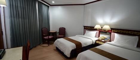 A hotel room with two beds, a desk, a chair, a lamp, and a telephone.