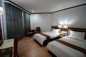 Two single beds with matching headboards, a desk, and a nightstand, set against a large window with curtains.