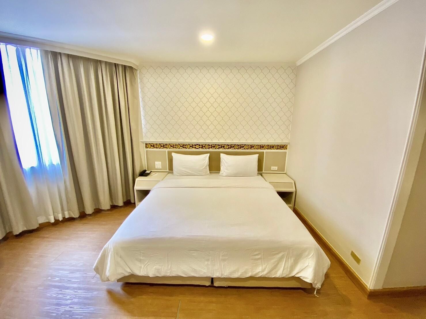 A hotel room with a large bed, two bedside tables, a nightstand, and a window with curtains.