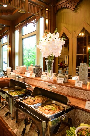 A buffet area with various food stations, a vase with white flowers, and a view of the outdoors through large windows.