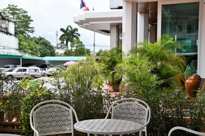 A patio area with two white metal chairs and a small round table, surrounded by potted plants and flowers.
