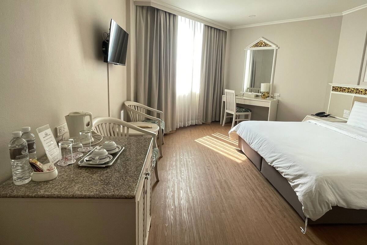 A hotel room with a bed, a desk with a chair, a television, and a window with curtains.