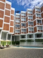 A modern hotel with a pool area, featuring a unique brick and white facade, multiple balconies, and outdoor seating.
