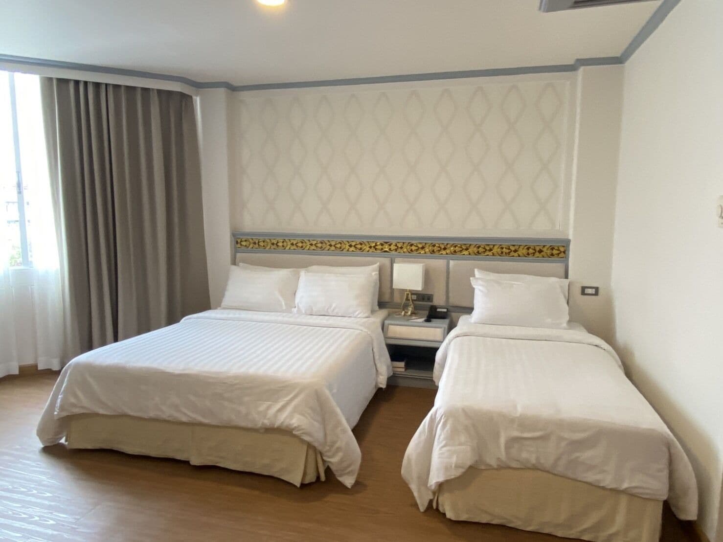 A hotel room with two beds, a nightstand, a lamp, and a patterned wall.