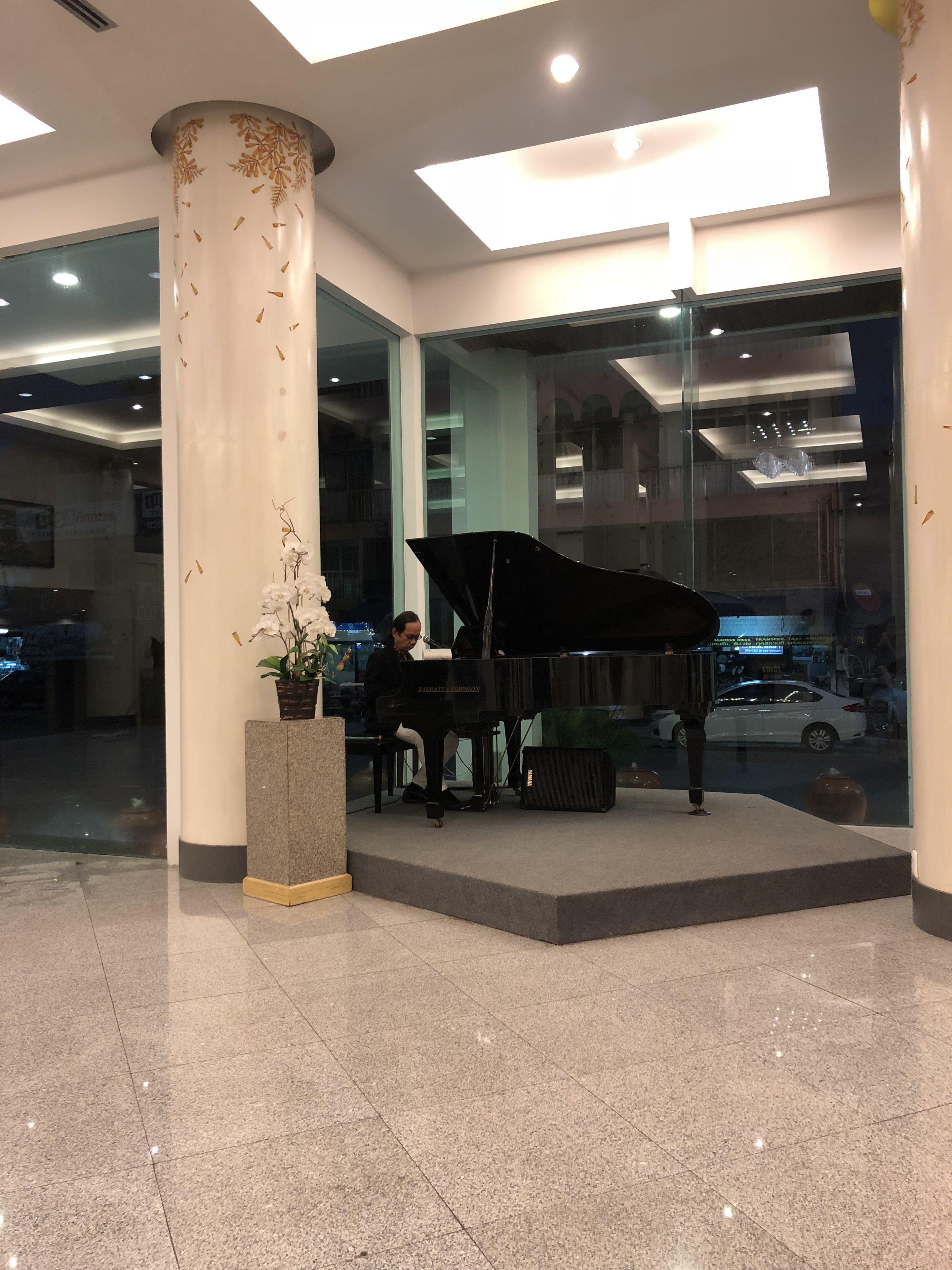 A grand piano in a lobby with a large pillar and a potted plant.