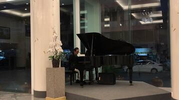 A grand piano in a lobby with a large pillar and a potted plant.