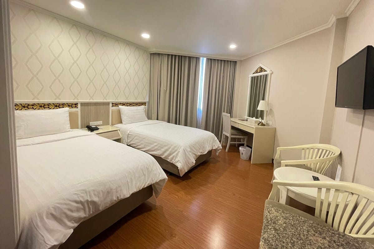 A hotel room with two beds, a desk, a chair, a TV, and a window with curtains.