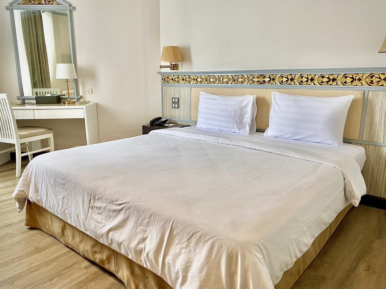 A neatly made bed with white linens, a desk with a lamp, and a telephone.