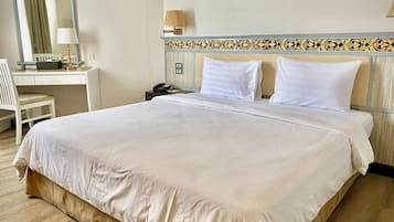 A neatly made bed with white linens, a desk with a lamp, and a telephone.