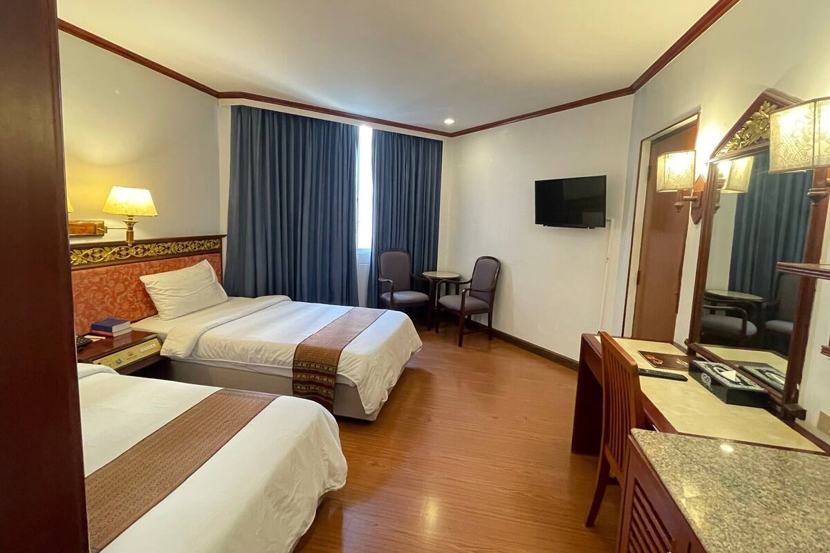 A hotel room with two beds, a desk, a chair, a television, and a large mirror.