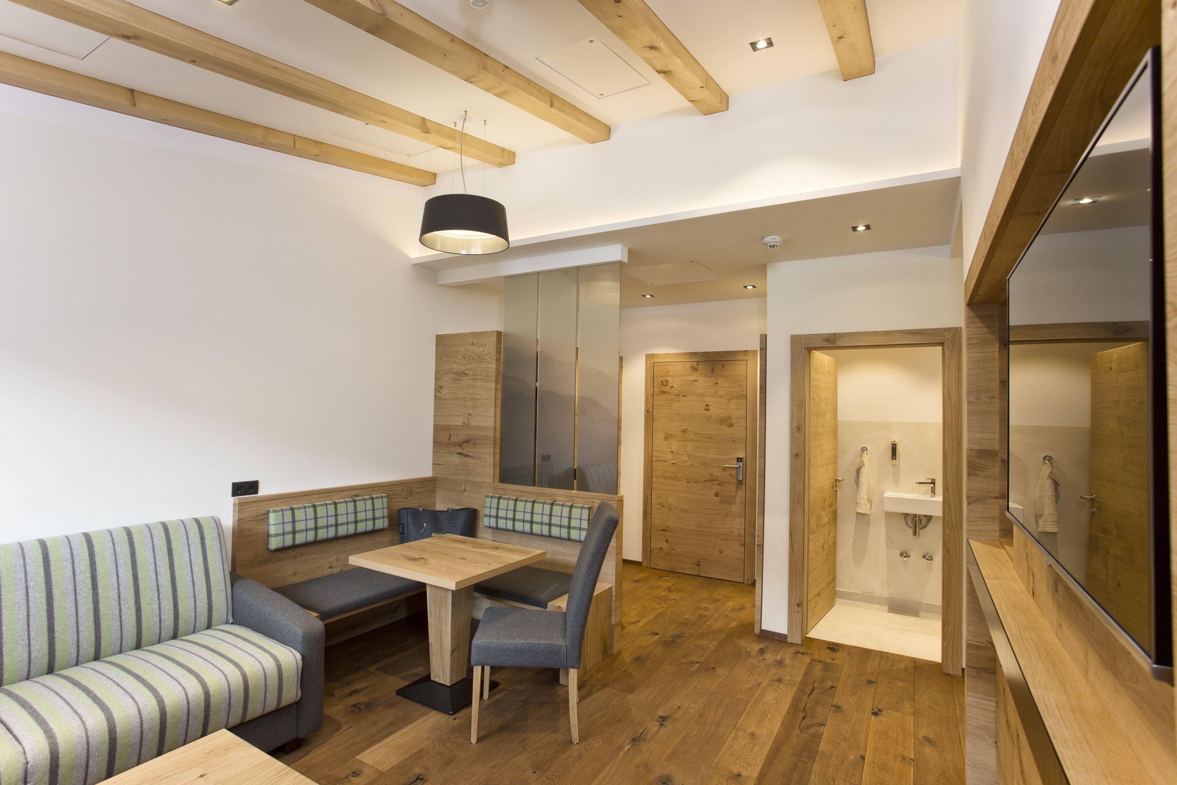 Un interior moderno con techo de madera, zona de comedor con mesa y sillas, sofá y baño con lavamanos y espejo.