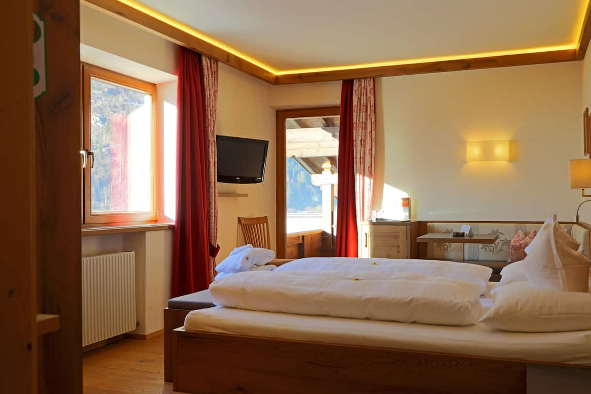 Een slaapkamer met een houten bed, een televisie, een bureau en een raam met gordijnen.