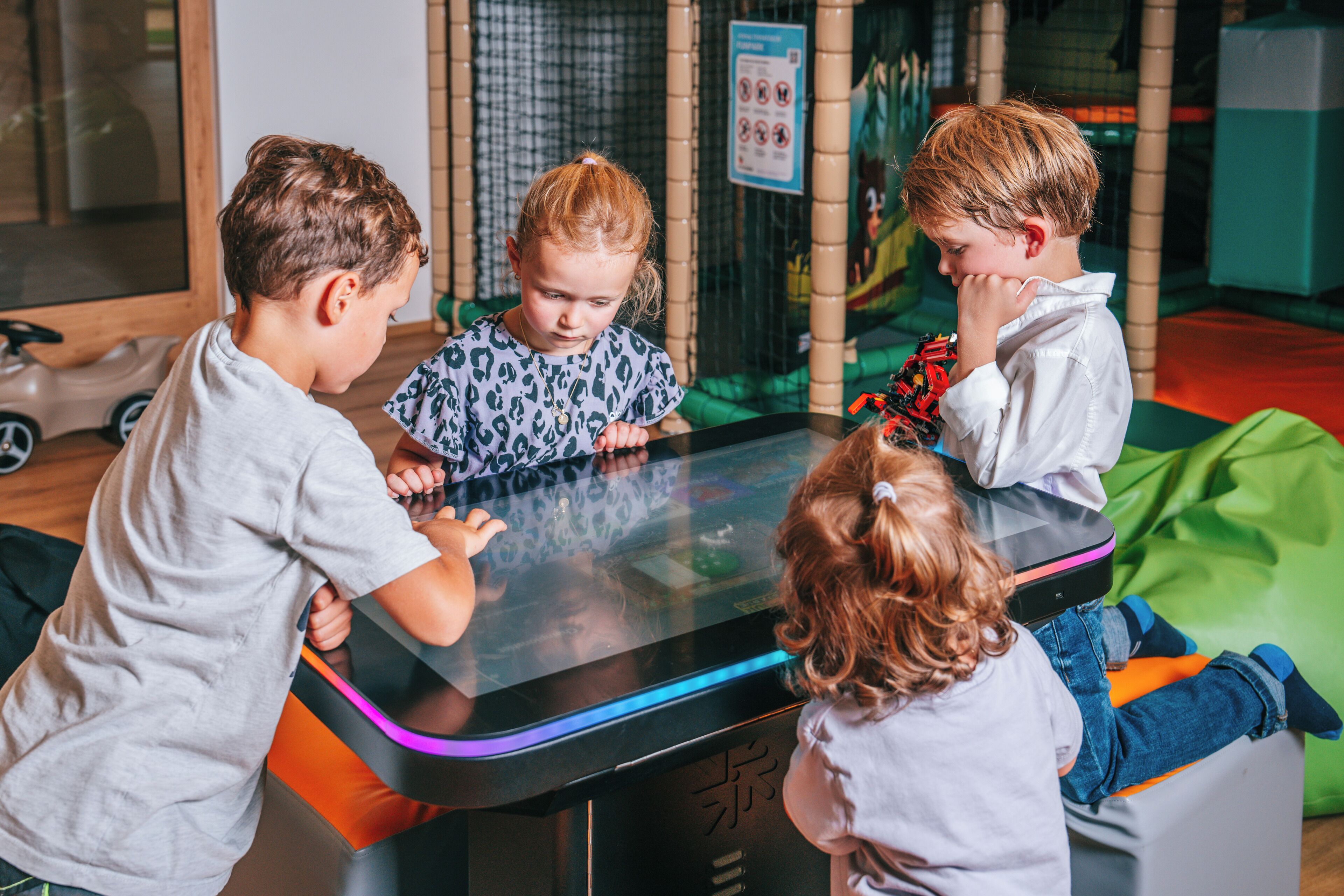 Four children interacting with a digital touchscreen display in an indoor play area.