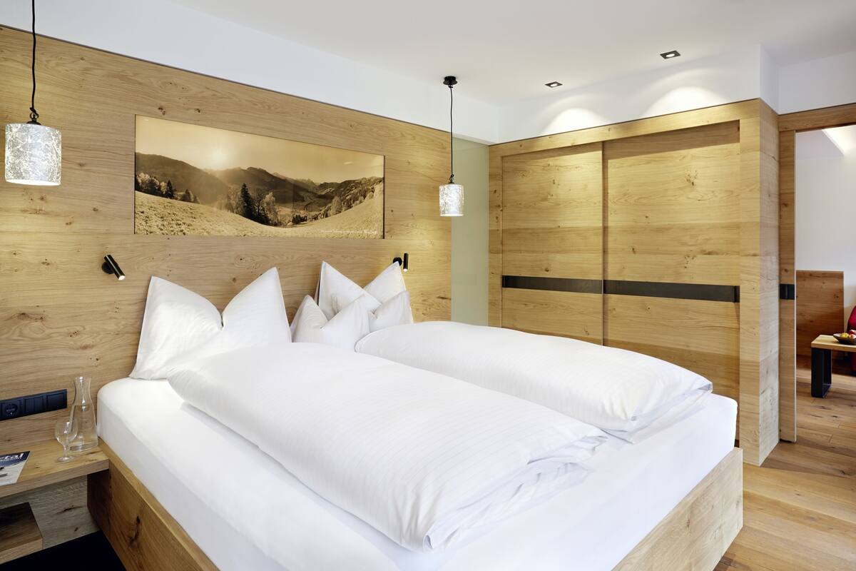 Een moderne slaapkamer met een houten hoofdbord, een groot bed met witte lakens, een hanglamp en een houten garderobe.