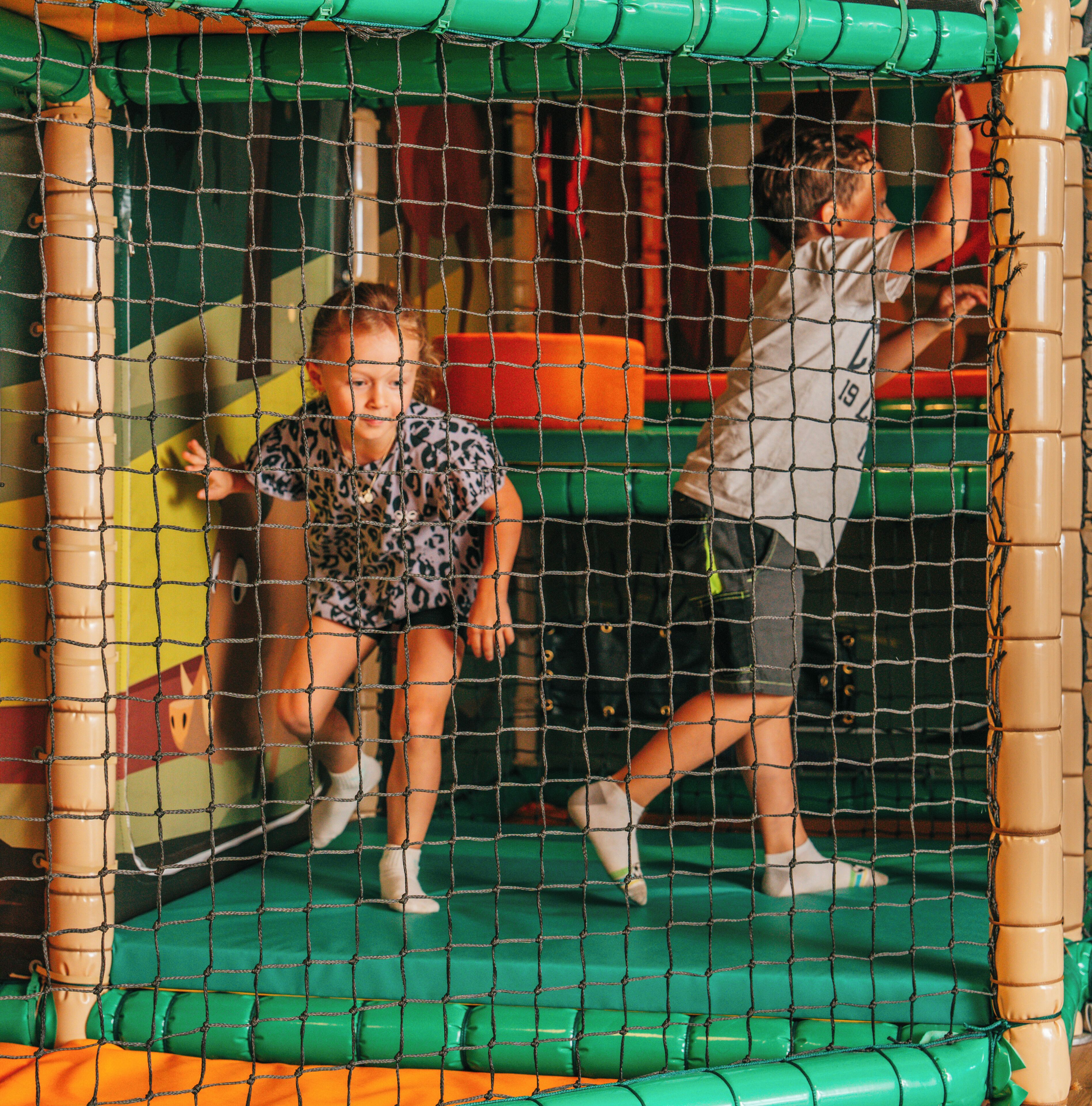 A play area with a netted enclosure, padded walls, and colorful padded structures.