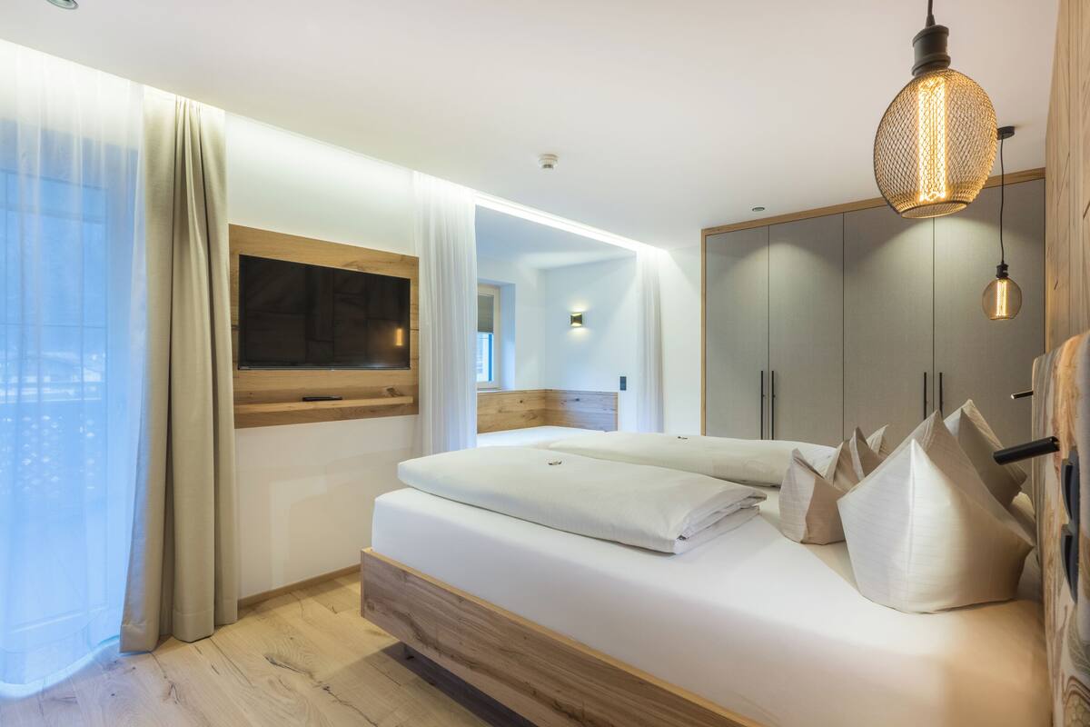 Een moderne slaapkamer met een bed, gordijnen, een televisie en een kledingkast.
