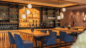 Un espacio de bar con estantes de madera, sillas azules y lámparas colgantes.