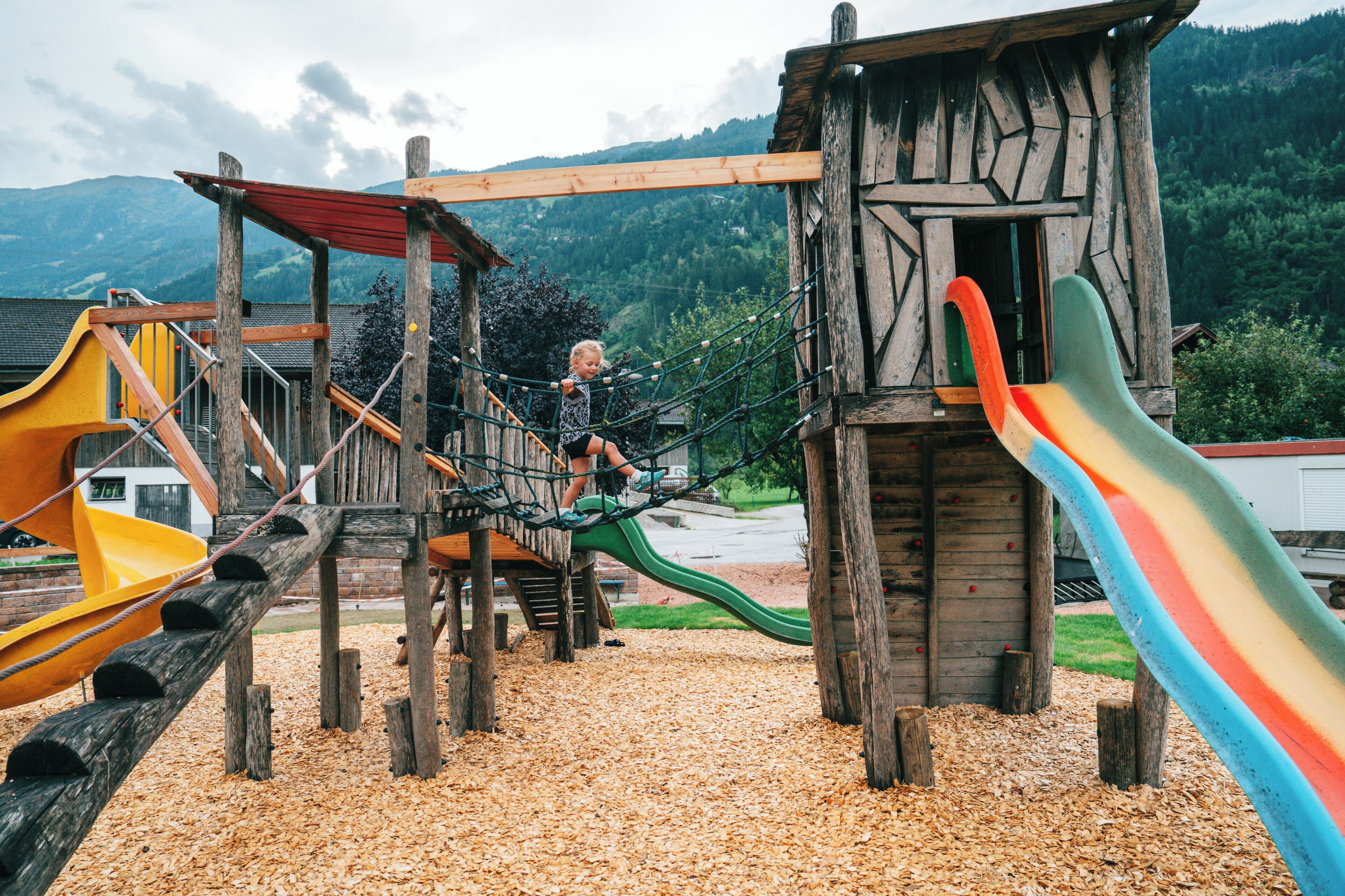 Ein Spielplatz mit Holzkonstruktionen, einer Rutsche und einer Hängebrücke.