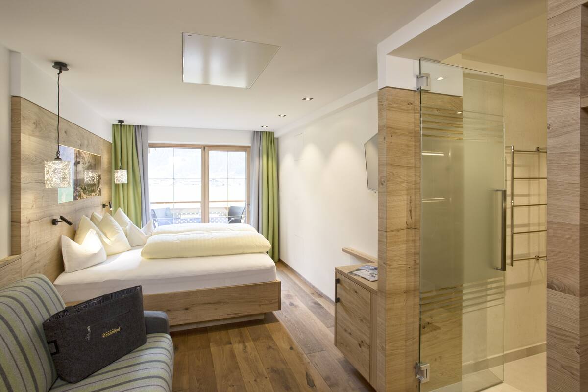 Een moderne slaapkamer met een bed, een slaapbank, een douchecabine van glas en een houten vloer.