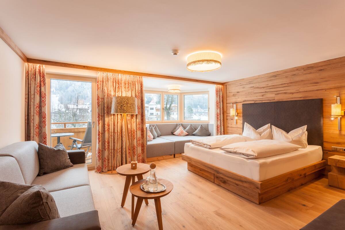 Een moderne hotelkamer met een groot bed, een bank, een eettafeltje en uitzicht op buiten.