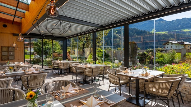 Un espacio para comer al aire libre con sillas y mesas de mimbre, y amplias ventanas con vistas a las montañas.