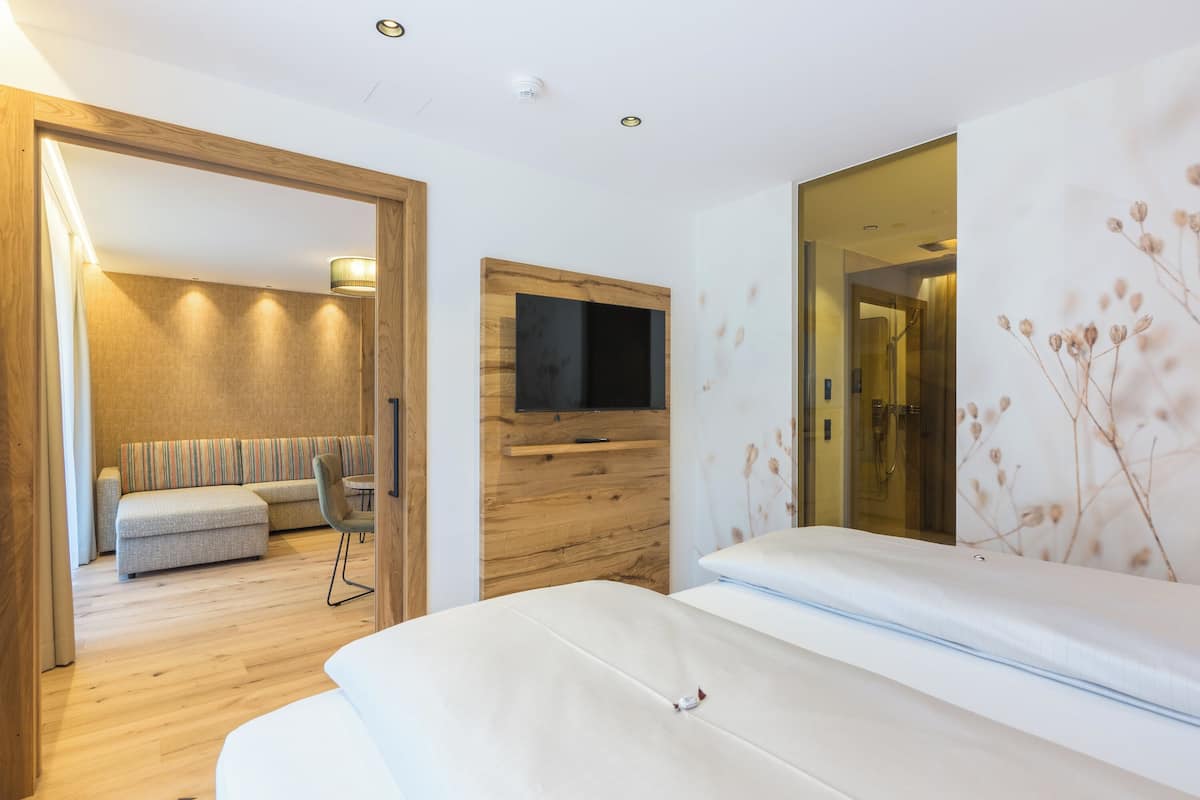Een moderne hotelkamer met een houten vloer, een bank, een bed, een televisie en een grote spiegel.